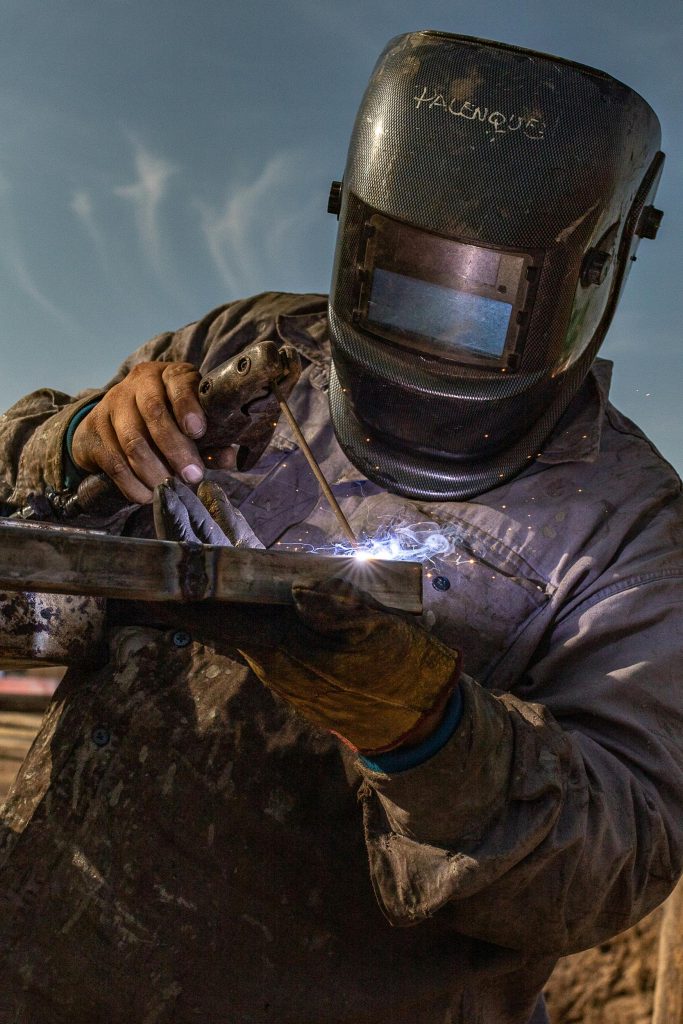 A welder in protective gear executes precise welding outdoors in Argentina.